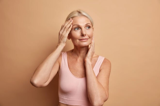 Sculptra After Menopause in Chicago Confident mature woman touching her smooth cheeks after Sculptra collagen treatment for menopause volume loss in Chicago