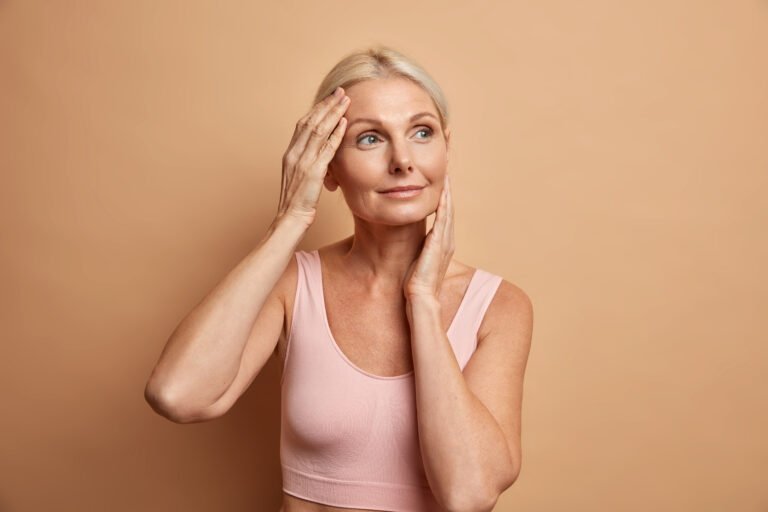 Sculptra After Weight Loss in Chicago Confident woman touching her smooth, fuller cheeks after Sculptra treatment for facial volume loss after weight loss