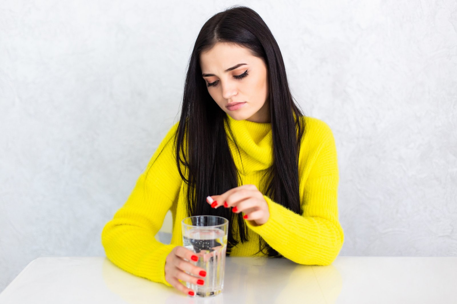 Woman taking a daily tablet with a small glass of water at home in the morning